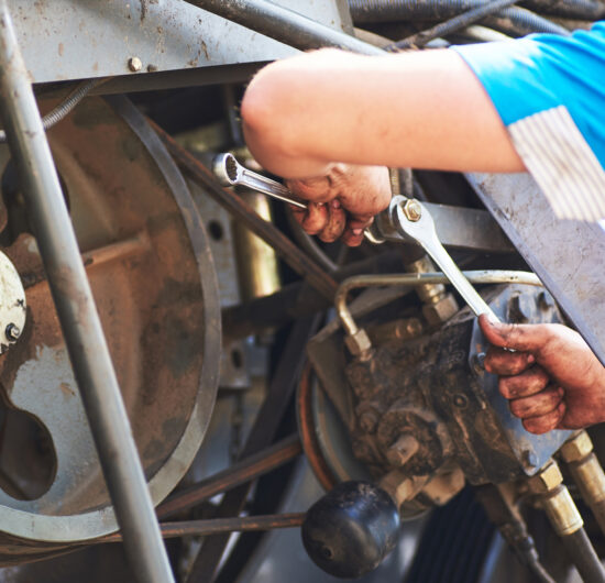 Combine machine service, mechanic repairing motor outdoors.