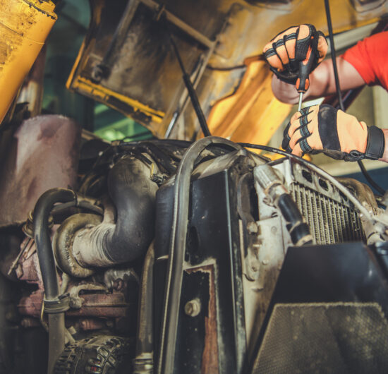 A mechanic is focused on repairing the engine of heavy machinery inside a workshop, ensuring everything is functioning properly.